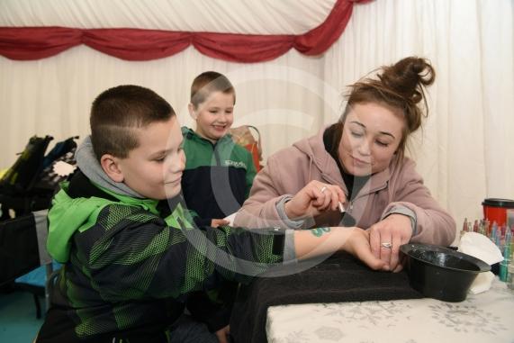 LtoR Adam Myga,10, has a glitter tattoo painted on his arm by Lucy Loomes, watched by his brother Szymon Myga, five. Slough Borough Council&rsquo;s Festive Fun event.Slough Town Square and Slough High Street.